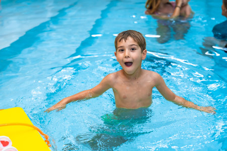 Young boy enjoying his summer vacation, playing and making funny faces in a swimming pool with a...