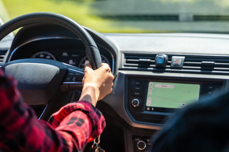 Woman driving a car, holding the steering wheel with left hand and using gps navigation on the...