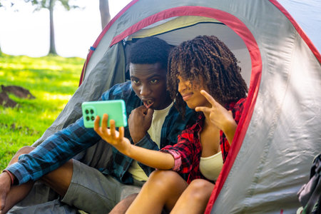 Two young campers are taking a selfie inside their tent, enjoying a moment of fun during their camping tripの写真素材