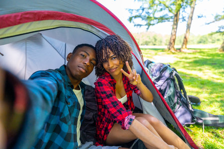 Young couple taking a selfie inside their tent while camping in nature, enjoying a relaxing vacationの写真素材