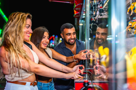 Group of friends having fun playing a crane game, trying to grab a prize, at an amusement park at...