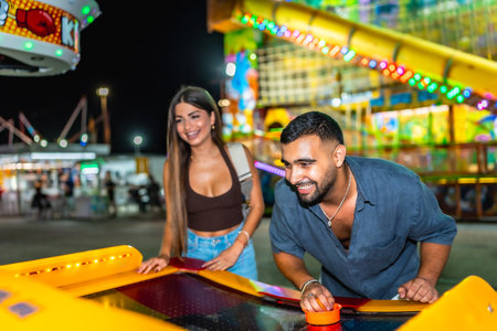 Young man and woman having fun playing air hockey at amusement park at night, enjoying their leisure time togetherの写真素材