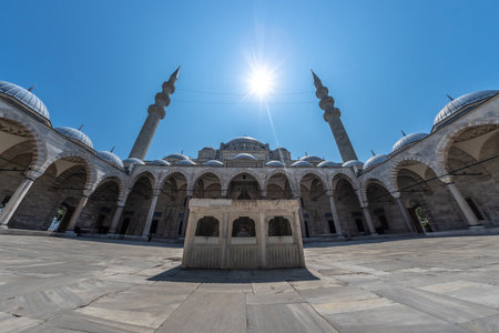 Wide angle view of the courtyard of Suleymaniye Mosque in Istanbul, Turkey, featuring intricate stonework, arches, domes, minarets, and the sun shining brightly overheadの写真素材