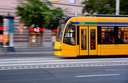 Yellow tram speeding through the bustling city center, showing motion blur and filled with passengers enjoying their commuteの写真素材