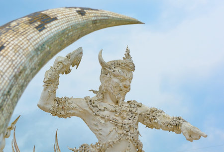 White statue of a mythological being with horns raising an arm towards a mosaic arch against a blue...