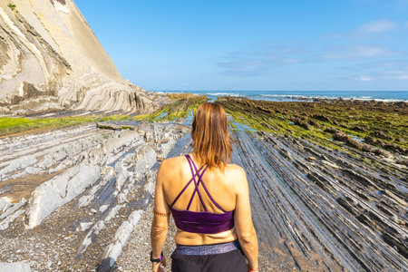 Female tourist exploring the unique geological formations of the flysch cliffs on sakoneta beach in...