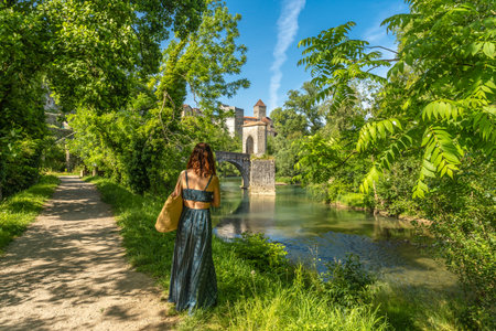 Tourist admiring the medieval bridge and the church of saint andre in sauveterre de bearn, a picturesque village in the pyrenees atlantiques region of franceの写真素材