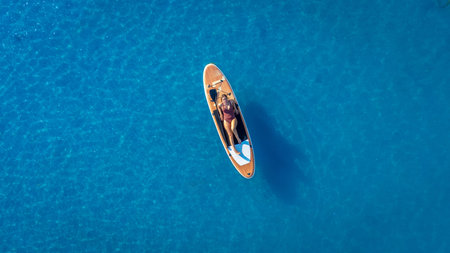 Person enjoys a sunny day paddle surfing on calm, clear blue water, capturing the essence of summer relaxation and outdoor adventureの写真素材