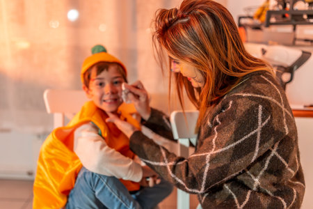 Mom applying colorful makeup on her son's face, creating a festive atmosphere for their Halloween party at home, filled with joy and excitementの写真素材
