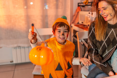 Happy child wearing pumpkin costume holding a plastic jack o' lantern celebrating halloween with family at homeの写真素材