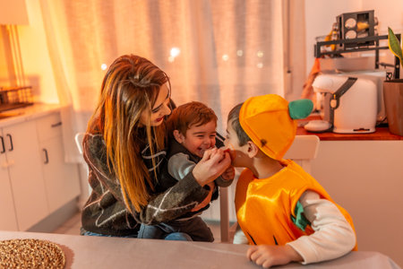 Children wearing pumpkin costumes celebrating Halloween joyfully with their mother at home, creating warm memories of togetherness and laughterの写真素材