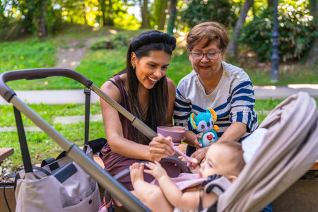 Grandmother, mother and baby girl enjoying time together at the park, feeding the baby girl and playing with a plush toyの写真素材