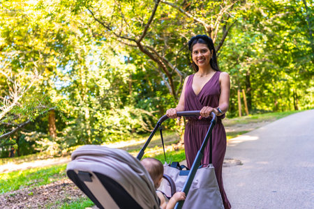 Latin mother enjoying a sunny summer day while walking in the park with her baby in a stroller,...