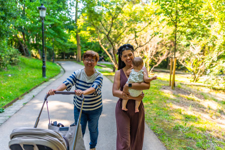 Happy latin family walking in a park, grandmother pushing a stroller and mother holding her babyの写真素材