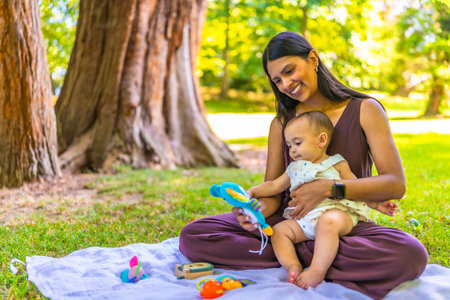 Latin mother and daughter enjoying a sunny day at the park, playing with colorful toys and creating a heartwarming family momentの写真素材