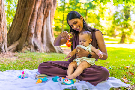 Latin mother holding her baby daughter and playing with colorful toys while sitting on a blanket in...