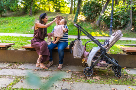 Three generations of a latin family enjoying time together in a park, with mother feeding her baby...