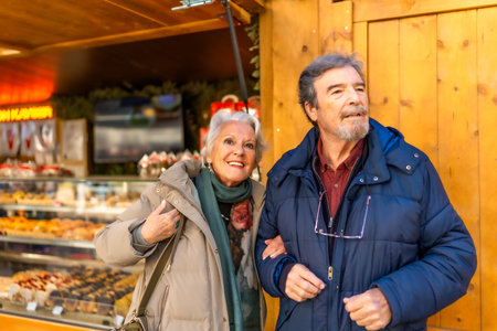 Happy senior couple strolling arm in arm at a traditional Christmas market, enjoying the festive atmosphere and holiday cheerの写真素材
