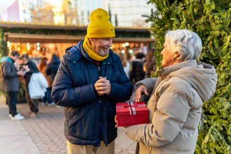 Elderly man and woman exchanging gifts at a Christmas market in the city during winter holidaysの写真素材