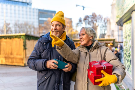 Cheerful senior couple holding christmas gifts and pointing at something interesting at the christmas market in the cityの写真素材