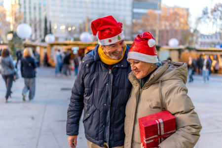 Smiling senior couple wearing santa hats holding hands and enjoying christmas market in the city during winter holidaysの写真素材