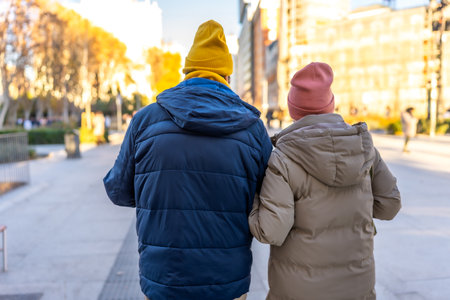 Elderly couple wearing winter clothes and colorful beanies enjoying a walk in a city park during wintertimeの写真素材