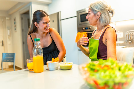 Senior woman wearing apron explaining recipe to her young adult daughter while preparing a healthy meal together in a modern kitchenの写真素材