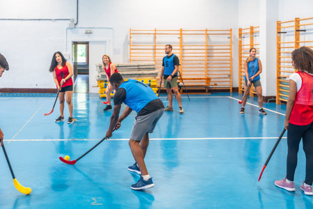 Floorball team players practicing passes during training inside a gym, skillfully hitting the ball with their sticks on the vibrant blue floor, showcasing teamwork and athleticismの写真素材