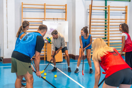 Floorball team practicing game strategy with their coach in a gymnasium, focusing on teamwork and...