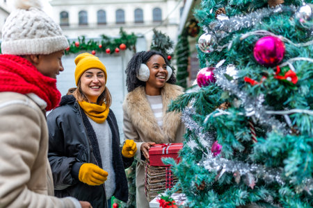 Three happy friends enjoying Christmas shopping at an outdoor market, choosing a Christmas tree and...