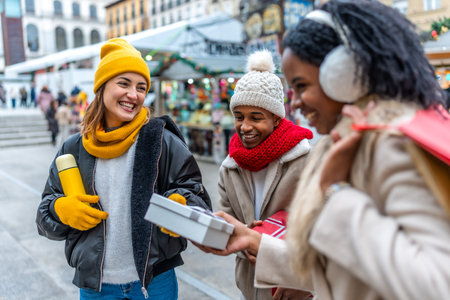 Multi ethnic friends exchanging gifts and smiling at a christmas market during wintertimeの写真素材