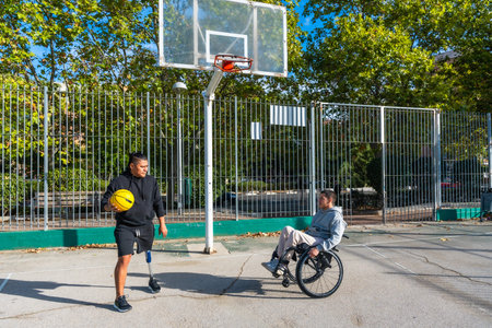 Disabled men, one using a wheelchair and the other wearing a prosthetic leg, playing basketball on...