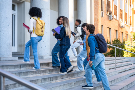 Diverse group of college students walking up campus stairs with backpacks and books, enjoying sunny day, teamwork and ambition as they head toward higher education and future successの写真素材