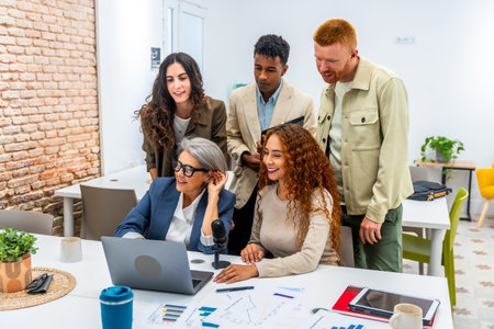 Diverse business team working together in a modern office, grouping around a laptop and microphone,...