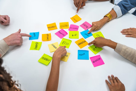Diverse business professionals collaborating, pointing at colorful sticky notes with written concepts on a white table, symbolizing teamwork, planning, and strategy in a corporate meeting settingの写真素材
