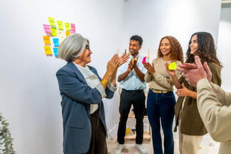 Diverse business people clapping hands in an office meeting room, celebrating a successful project achievement or a senior female manager's accomplishment, demonstrating teamwork and appreciationの写真素材
