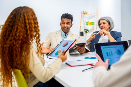 Business professionals discussing financial data and charts on digital tablets and paper during a...