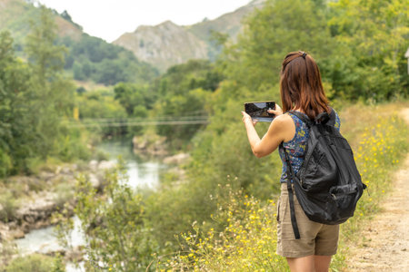Female tourist with a backpack capturing photos of the Dobra river along the scenic route to Olla de San Vicente in Asturias, Spain, on a sunny summer dayの写真素材