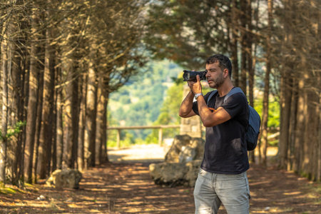 Male photographer taking pictures with professional camera in a forest near a viewpoint in Benia de Onis, Asturias, Spain, during a sunny summer dayの写真素材