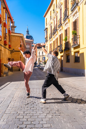 Two energetic young men performing a street dance on a cobblestone street in a lively European urban setting under clear blue skies, expressing creativity and freedomの写真素材