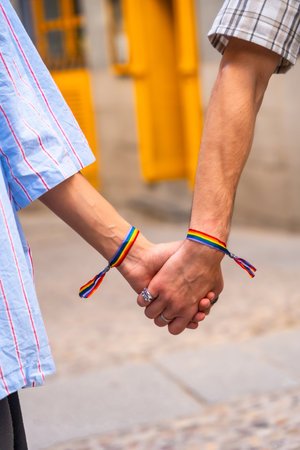 Couple's hands holding together, both wrists featuring rainbow bracelets, symbolizing love, pride, and support for the lgbtq plus community, representing equalityの写真素材