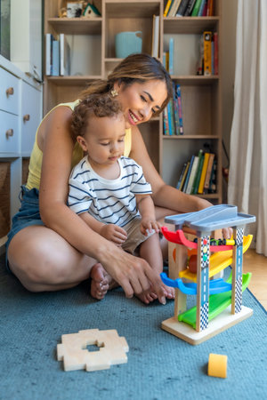 Smiling mother and son playing with a toy car and garage, enjoying quality time together in their...