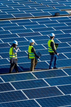 Engineers wearing safety vests and hard hats are walking across a vast array of solar panels at a...