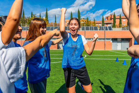 Excited female soccer players celebrating success and victory together, raising their arms in retirement on a green artificial turf field after a gameの写真素材