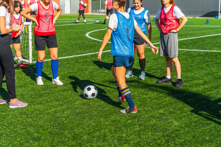 Diverse women soccer players training together on a sunny outdoor turf field, practicing dribbling, passing and teamwork to build fitness, skill and competitive confidenceの写真素材