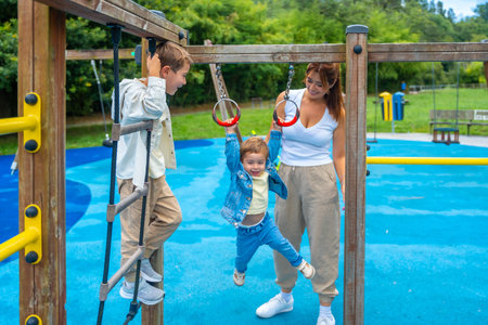 Two brothers and their mother are having fun on a playground jungle gym, with one child climbing a...
