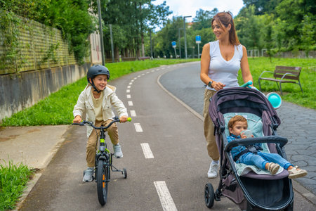 Happy mother walking with her two children, one riding a bicycle with training wheels and the other...