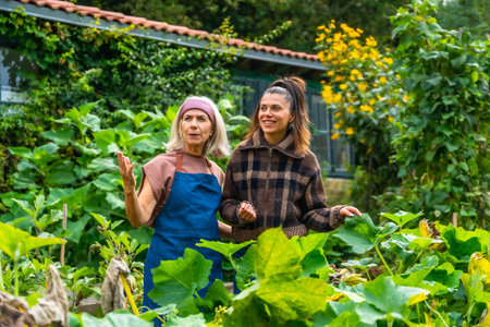 Mother and adult daughter enjoying time together in a lush green garden, the older woman teaching and sharing her gardening experience with the younger womanの写真素材