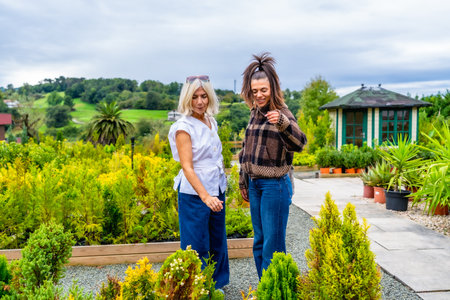 Mother and daughter browsing potted plants and small trees at a garden center, enjoying a relaxed day together selecting greenery and sharing a warm, casual moment outdoorsの写真素材