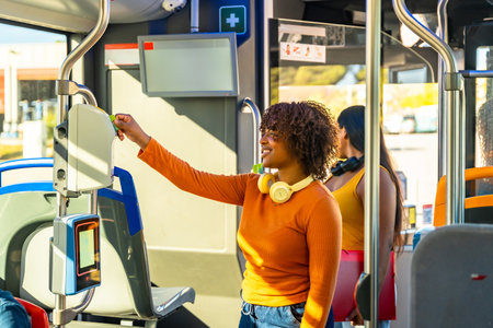 Happy young woman passengers using a smart card on an electronic validator, paying for a journey on public transport, demonstrating modern urban commuting solutionsの写真素材